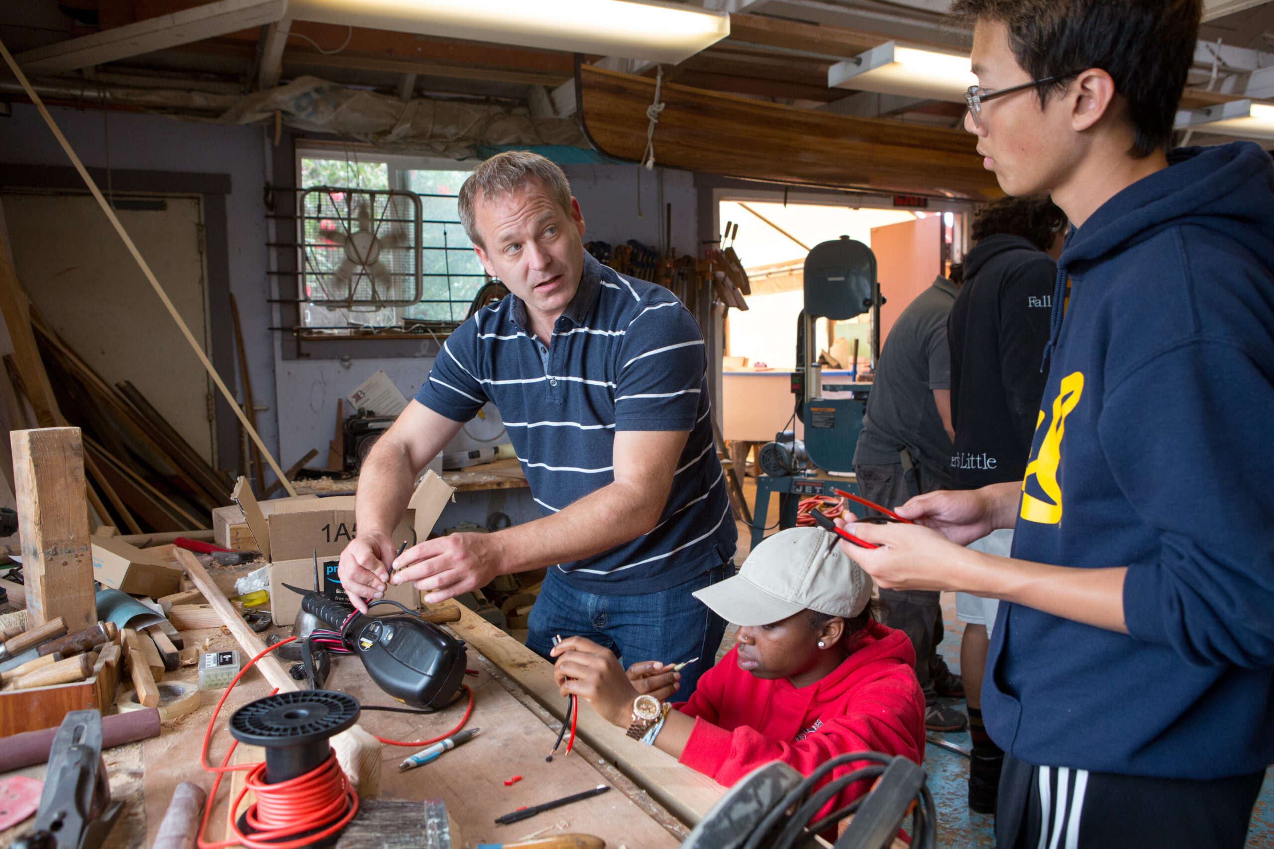 A teacher helps students wire the motor for a solar-powered boat.